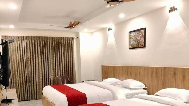 Habitación de hotel con dos camas, un ventilador de techo, un cuadro en la pared y una cortina.