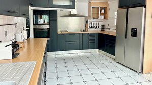 Une cuisine moderne avec des meubles de couleur sombre, un réfrigérateur en acier inoxydable et un sol carrelé.