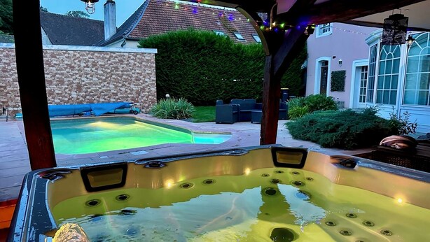 Un bain à remous offrant une vue dégagée sur une piscine et un espace patio aménagé avec du mobilier d’extérieur.