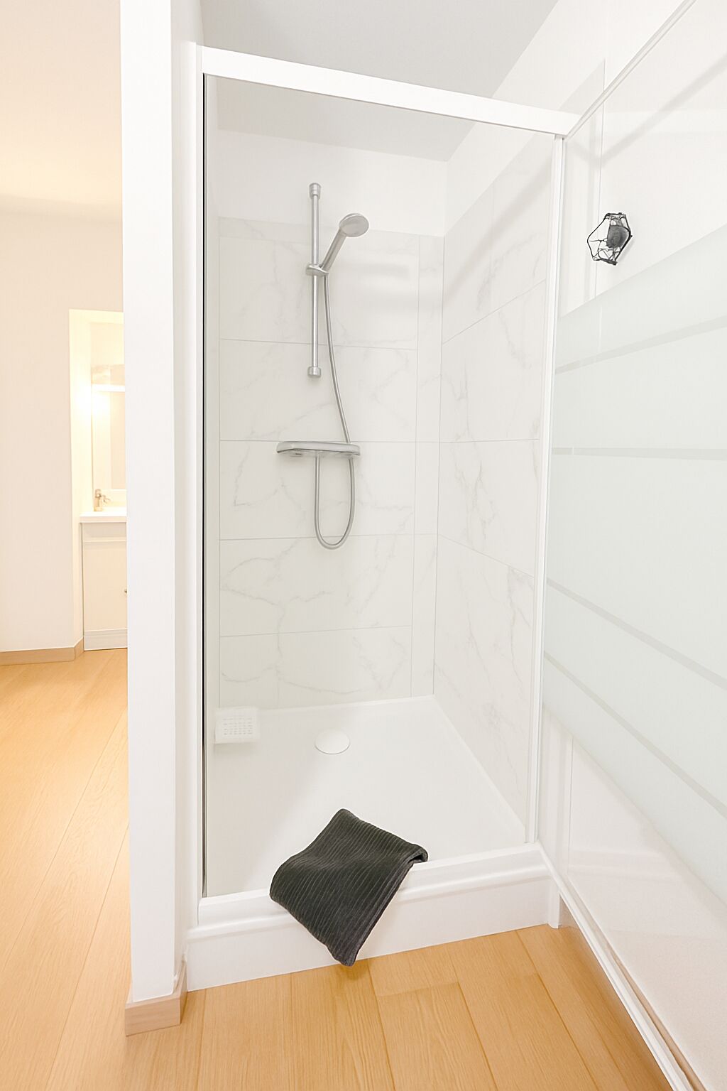 A modern shower with a glass door, a handheld showerhead, and a handheld showerhead.