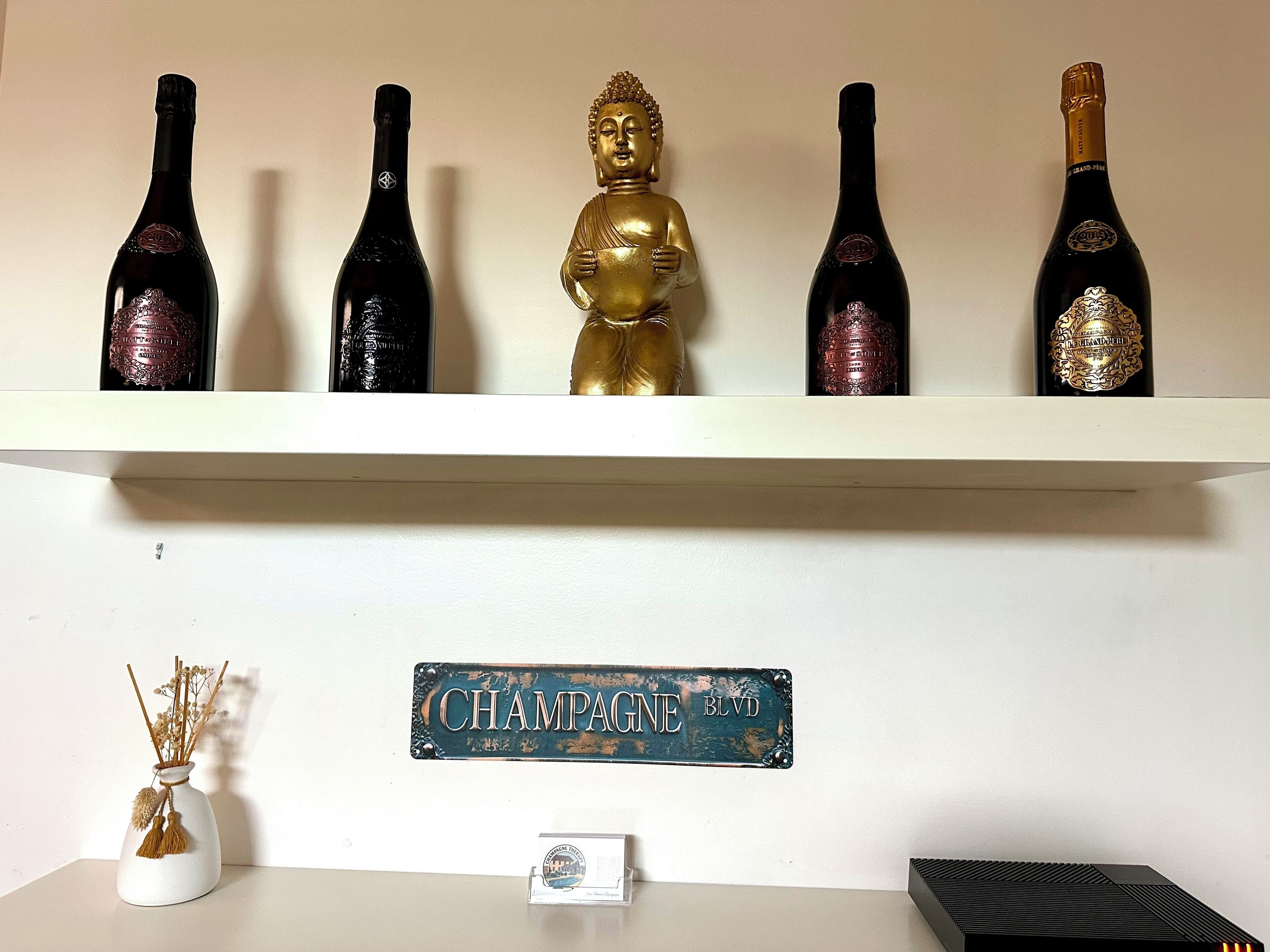 A shelf with wine bottles and a Buddha statue. Below, there's a sign reading "CHAMPAGNE BLVD."