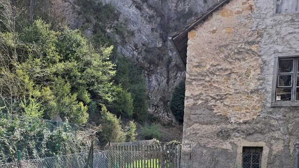 A stone building with a rustic exterior, a table with chairs, and a fenced garden area with trees and shrubs. - Ideal for hikers, artists and nature lovers (Waldenburg)