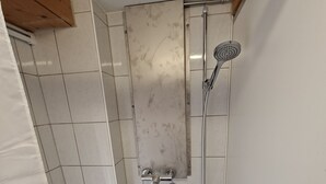 A small bathroom with white tiled walls, a shower with a handheld showerhead, and a blue-tiled floor. - Ideal for hikers, artists and nature lovers (Waldenburg)