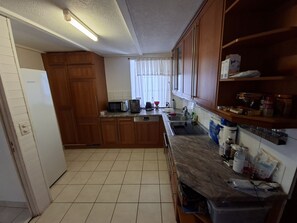 Uma cozinha com armários de madeira, micro-ondas, pia e diversos utensílios sobre a bancada.