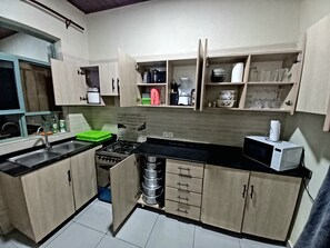 A compact kitchen with a gas stove, sink, and a microwave. There are cabinets with various kitchen utensils and appliances.