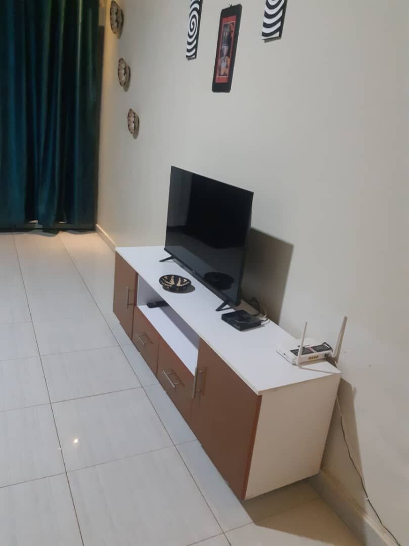 Una habitación con un escritorio blanco, un televisor de pantalla plana, una computadora portátil y un enrutador.