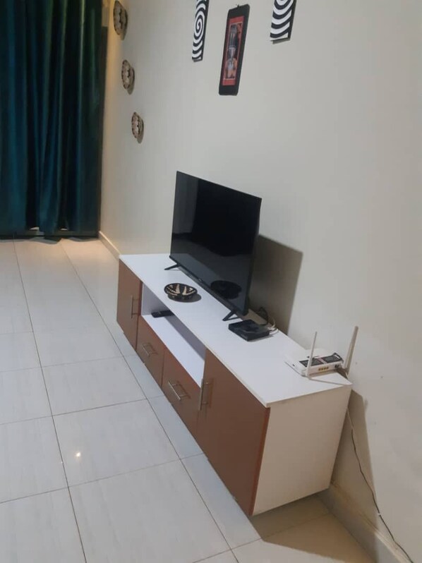 A room with a white desk, a flat-screen TV, a laptop, and a router.