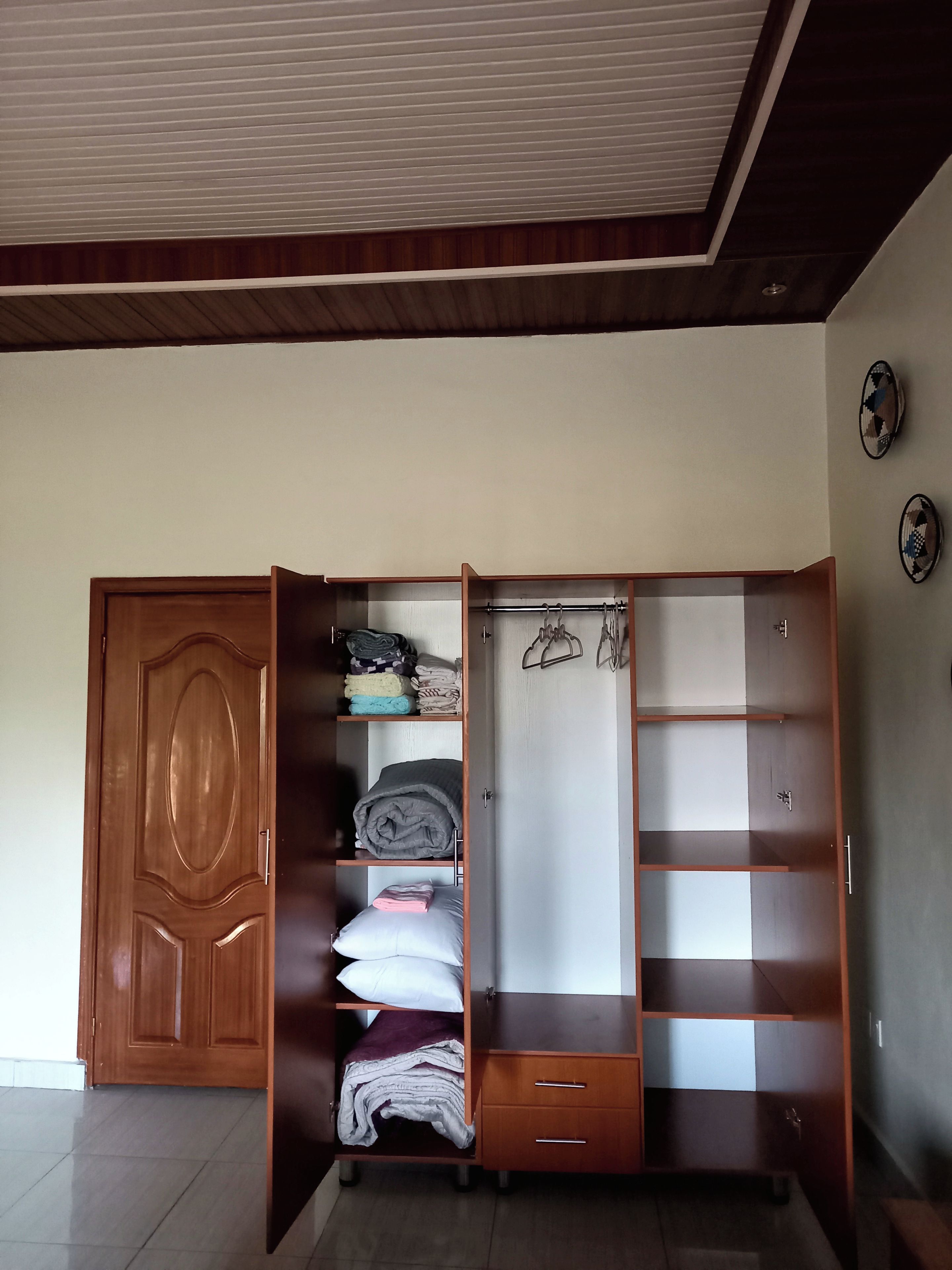 A room with a wooden wardrobe, a bed with pillows, and a tiled floor.