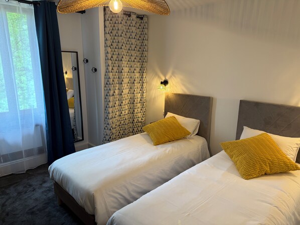 Habitación de hotel con dos camas, un ventanal con cortinas, un papel tapiz decorado y una lámpara en el techo.