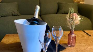 Una mesa de madera con un cubo blanco, dos copas de vino, un jarrón con flores secas y una botella de champán.