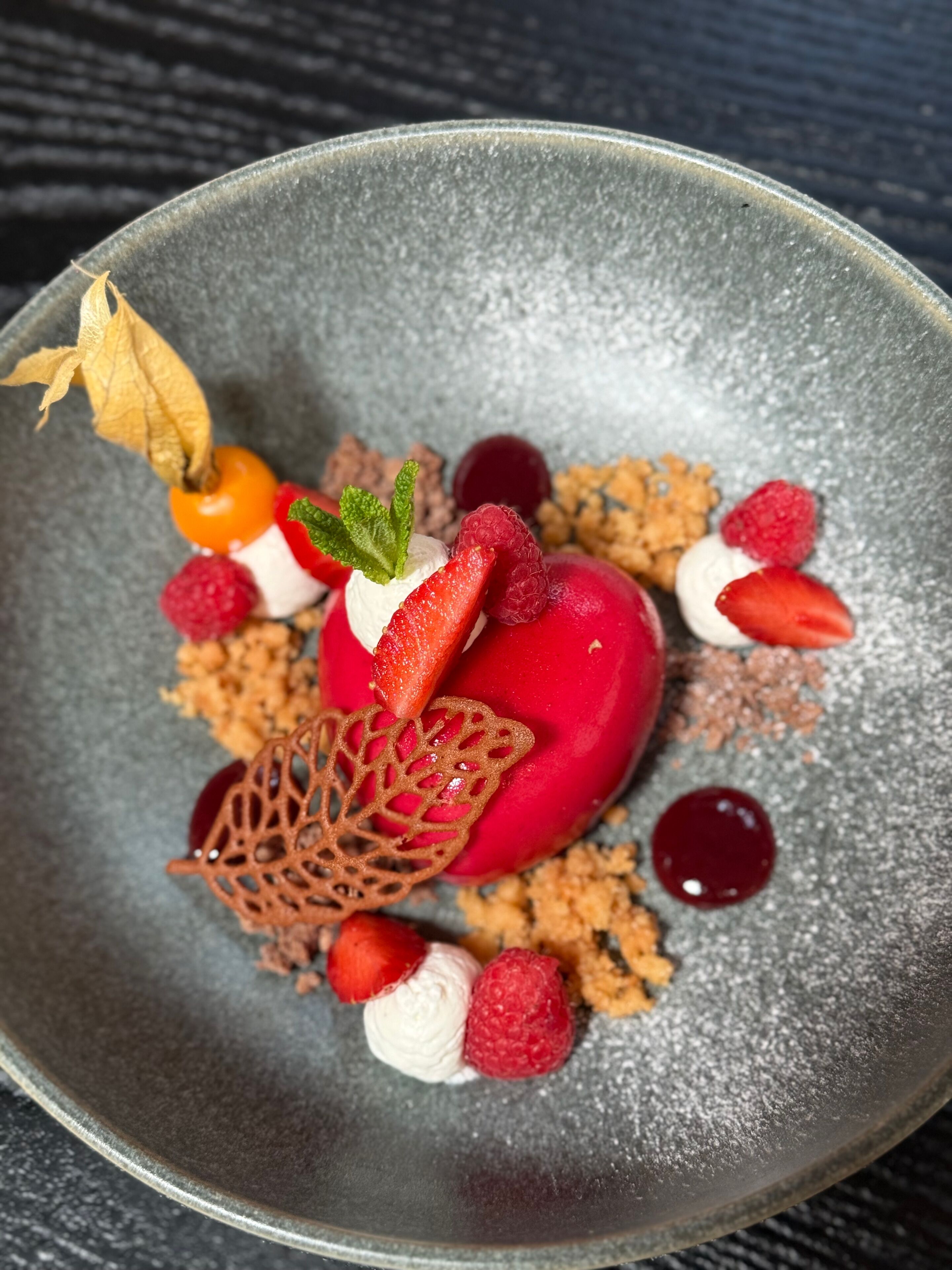 A dessert with strawberries, raspberries, and a decorative leaf on a plate.