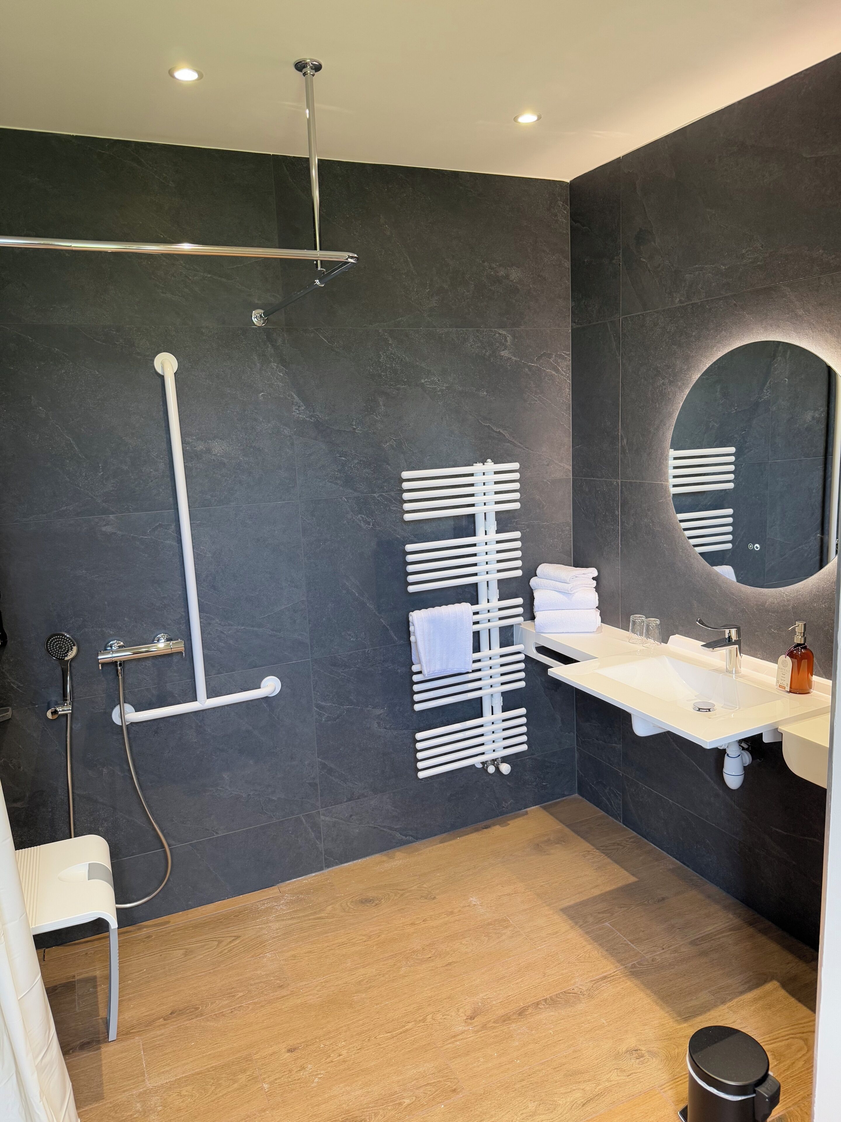 Un baño moderno con ducha, lavamanos, espejo y perchero para toallas.