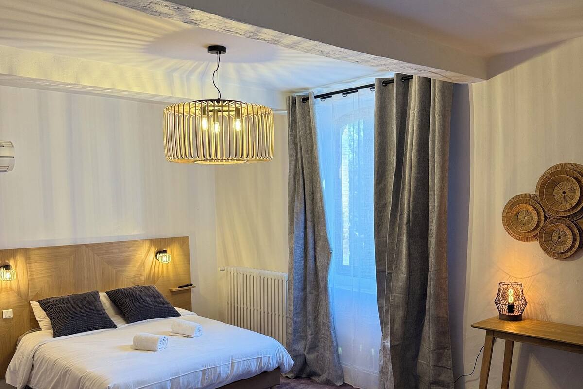 A bedroom with a bed, a sofa, a table with a lamp, and a window with curtains.