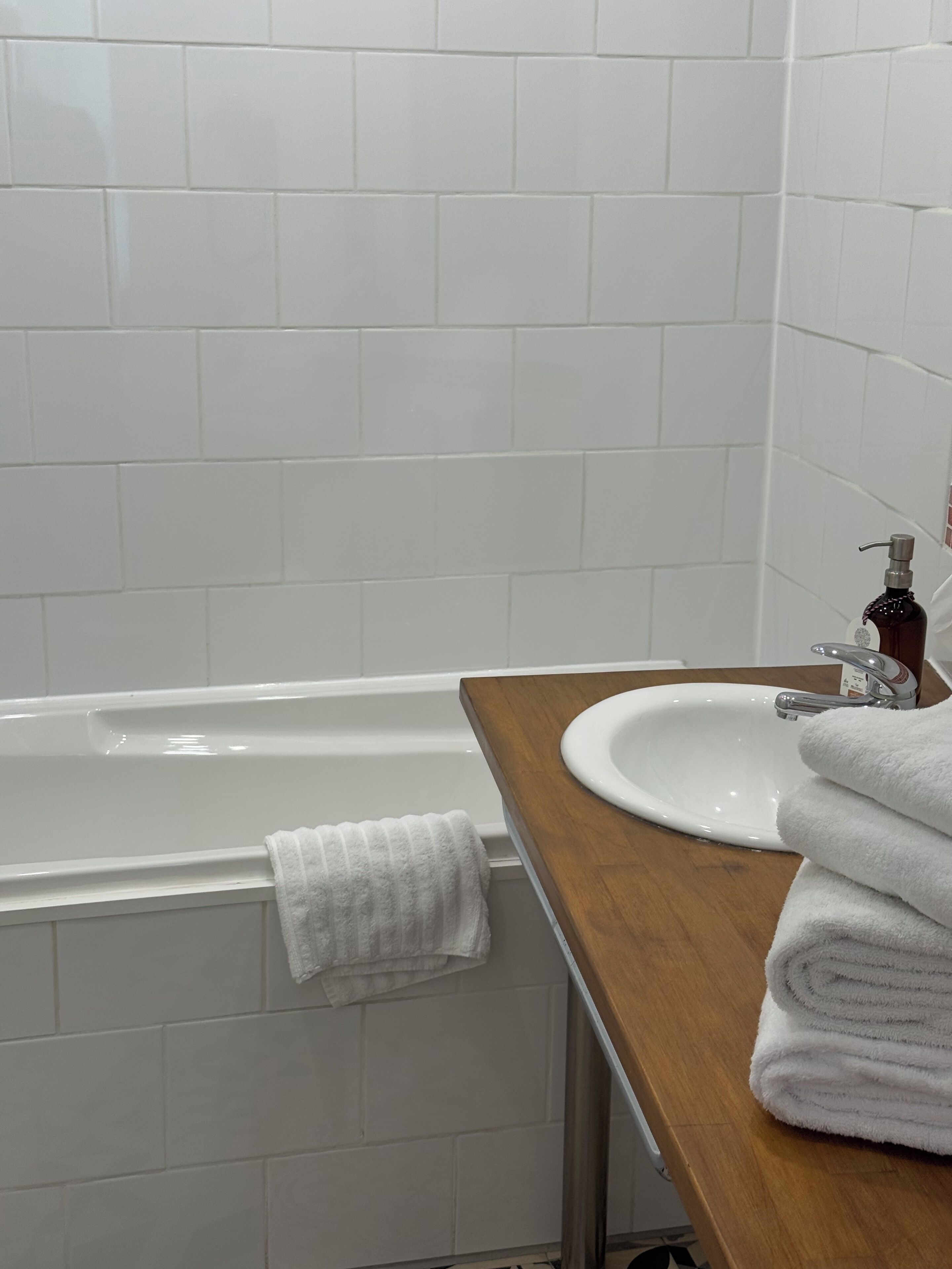 Un baño con una bañera blanca, un tocador de madera con un lavabo y un perchero para toallas.