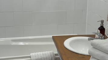 Un baño con una bañera blanca, un tocador de madera con un lavabo y un perchero para toallas.