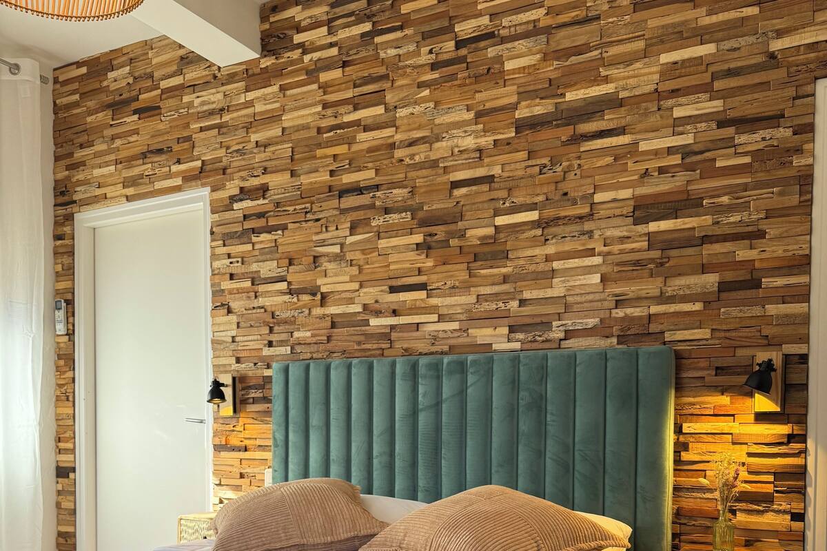 A bedroom with a wooden wall panel, a green upholstered headboard, and a bedside table with a vase.