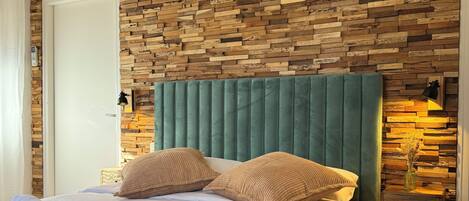 Un dormitorio con paneles de madera, un cabecero tapizado de color verde y una mesita de noche con un jarrón.
