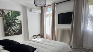 A bedroom with a bed, a mounted TV, an air conditioning unit, a radiator, and a window with curtains. - hotel restaurant LEs Boissières (Bioule)