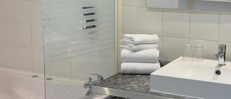Un baño con ducha envuelta en vidrio, un lavamanos blanco y un espejo sobre él.