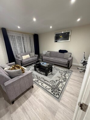 A modern living room with two grey sofas, a glass coffee table, a patterned rug, and a framed picture on the wall. - 3bed 2bath house/Entire house/Hi Speed WiFi/ Free Parking/Workstation/Garden (London)