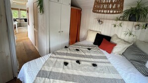 A bedroom with a large bed, a wardrobe, a hanging wicker chair, and a view of the outdoors. - Tiny house with terrace, beach chair and garden near Zingst (Pruchten)