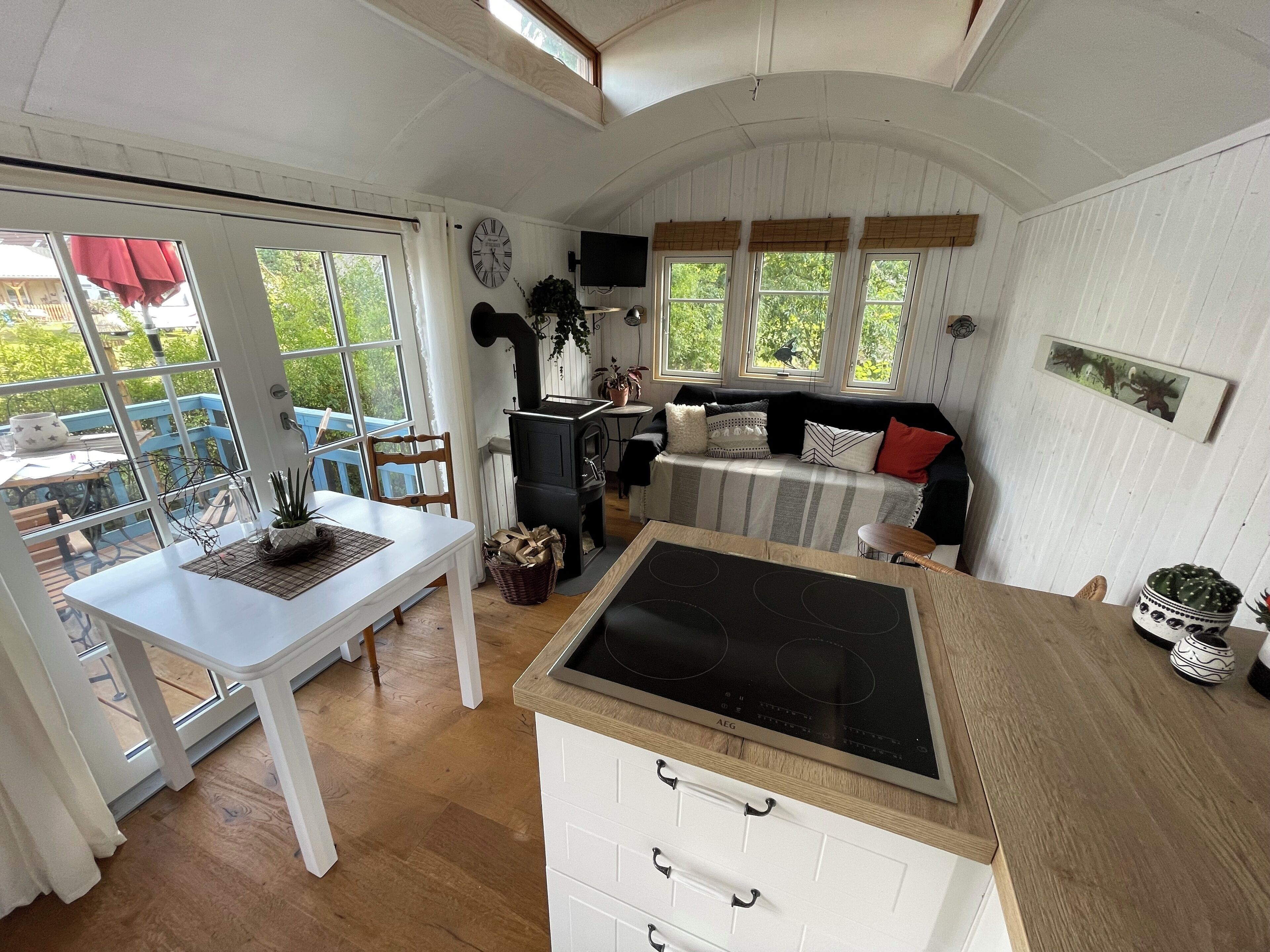 A cozy interior with a dining area, a kitchen with a stove, and a seating area with a sofa and windows.