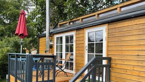 A wooden deck with a table and chairs, a red umbrella, and a staircase leading to a door. - Tiny house with terrace, beach chair and garden near Zingst (Pruchten)
