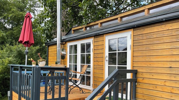 A wooden deck with a table and chairs, a red umbrella, and a staircase leading to a door. - Tiny house with terrace, beach chair and garden near Zingst (Pruchten)