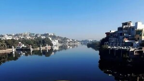 A mug with a white body and yellow interior, placed in front of a scenic view of a calm river with buildings on the opposite bank.