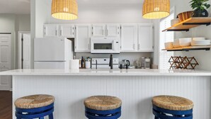 Une cuisine moderne avec des meubles blancs, un îlot central doté de tabourets et deux suspensions en osier.