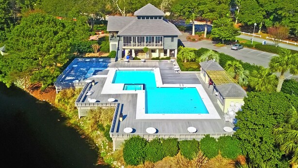 Une grande maison avec une piscine, entourée d’une végétation luxuriante et offrant une vue sur un plan d’eau.