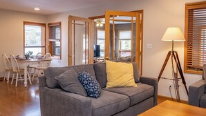 A living room with a grey sofa, a wooden floor, a dining area with a table and chairs, and a lamp. - Spacious Mountain Home with Private Hot Tub (Granby)