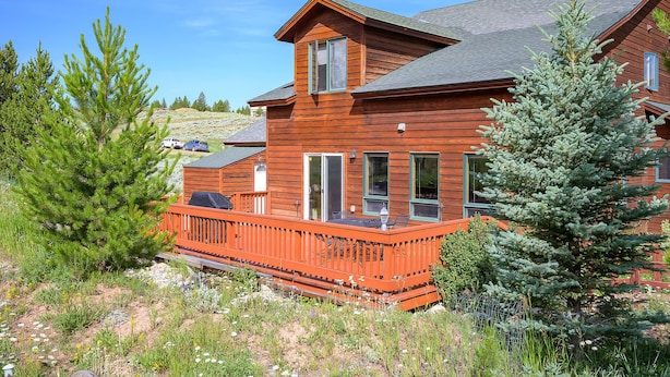 A two-story wooden cabin with a balcony, surrounded by greenery and a clear sky. - Spacious Mountain Home with Private Hot Tub (Granby)