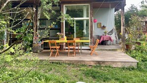 A wooden deck with outdoor furniture, a glass door entrance, and a view of the surrounding greenery. - Bright, quiet apartment with terrace and large natural garden. Lake and train station nearby (Utting am Ammersee)