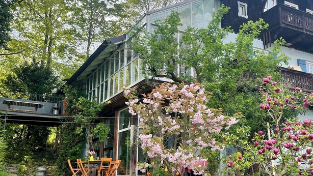 A modern house with large windows, a wooden deck, and a garden with various plants and flowers. - Bright, quiet apartment with terrace and large natural garden. Lake and train station nearby (Utting am Ammersee)