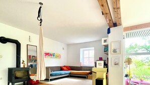 A cozy living room with a wooden floor, a sofa, a small TV, and a hanging chair. - Bright, quiet apartment with terrace and large natural garden. Lake and train station nearby (Utting am Ammersee)