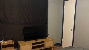 Een slaapkamer met een bed, een tv op een houten standaard, een deur en een donker gordijn.