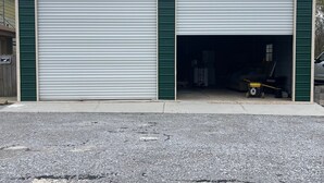 Een garage voor twee auto's met een grindpad en een houten omheining ervoor.