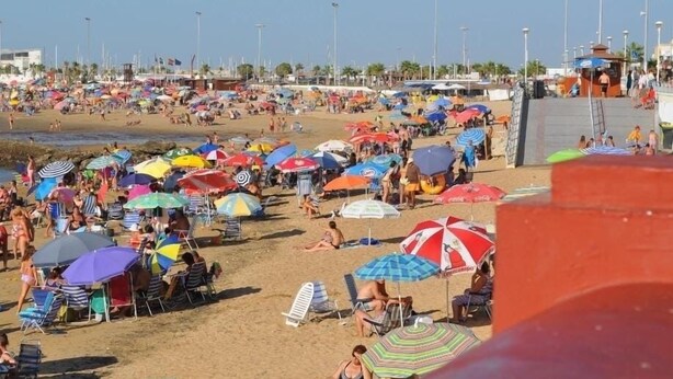 Une plage bondée, avec de nombreux parasols colorés et des chaises de plage.