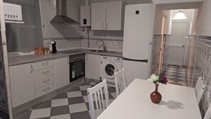 Une cuisine compacte avec des meubles blancs, un four encastré, un lave-linge et un coin repas comprenant une table et des chaises.