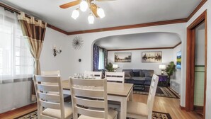 Un coin repas avec une table et des chaises en bois, un ventilateur de plafond et une vue sur le salon.