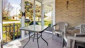 Un balcon avec une table et des chaises, un mur en briques et une vue sur la rue et la verdure.