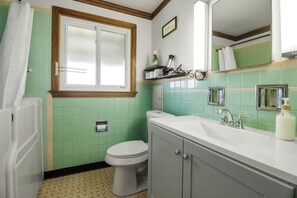 A bathroom with green tiles, a white toilet, a white sink with a mirror, and a shower curtain.