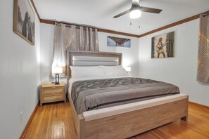 A bedroom with a bed, nightstand, lamp, ceiling fan, and artwork on the walls.