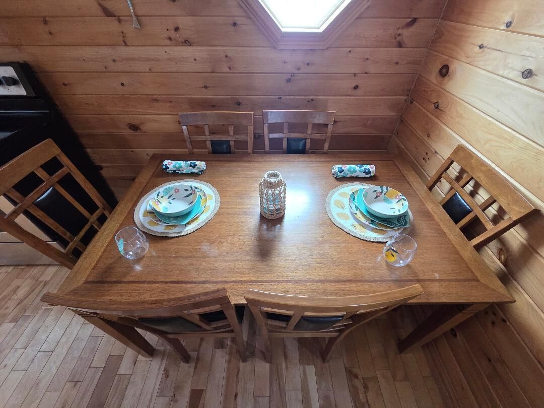 Una mesa de comedor de madera con cuatro sillas, un florero decorativo y un tragaluz arriba.
