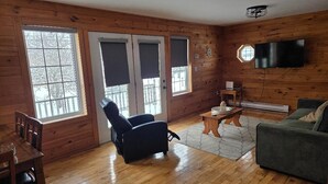 A wooden-paneled room with a dining table, a black chair, a green sofa, a TV, and a window with blinds. - Cozy House/Cottage, minutes to National Park & Golf Course (York)