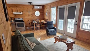 A cozy cabin interior with a wooden interior, a sofa, a dining table with chairs, a kitchen area, and large windows. - Cozy House/Cottage, minutes to National Park & Golf Course (York)