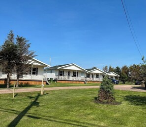 A row of single-story mobile homes with attached porches, a well-maintained lawn, and a clear blue sky. - Cozy House/Cottage, minutes to National Park & Golf Course (York)
