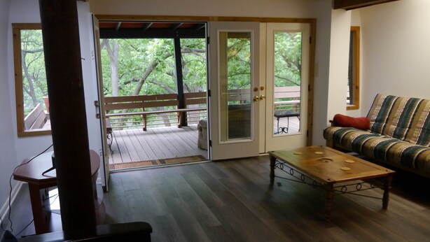 A living room with a wooden floor, a sofa, a coffee table, and a sliding glass door leading to a deck.