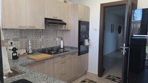 A kitchen with light wood cabinets, a gas stove, a built-in oven, and a black refrigerator. - A rare pearl (Oran)